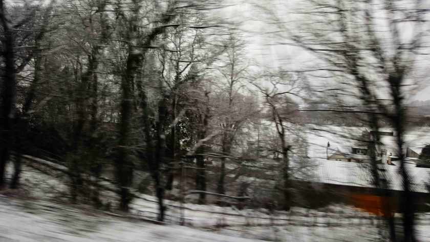 A blurry view of a snow covered wintry landscape with red sided building.