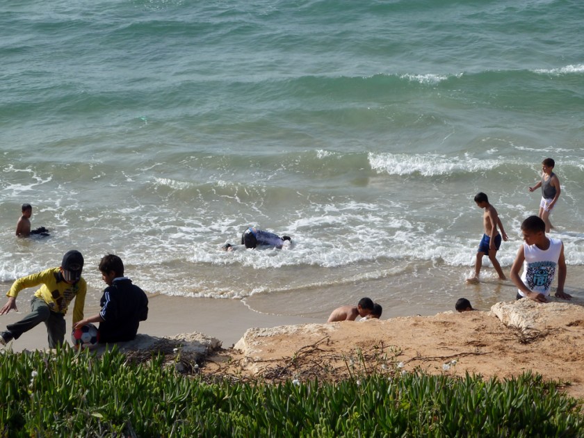 Boys play in the surf at the beach, one kneeling with his head underwater