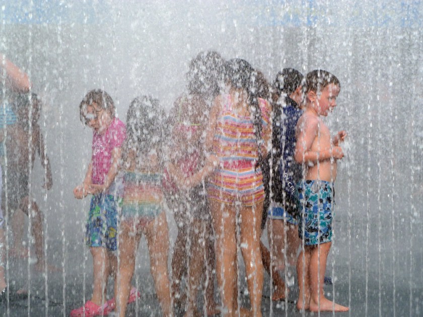 Children play in the spray of a sprinkler