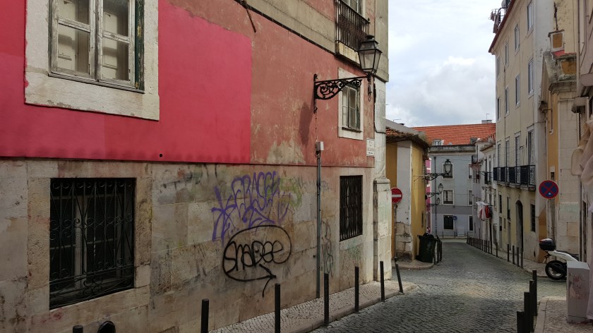 Cobble stone Lisbon street with plaster buildings grafittied and painted bright pink