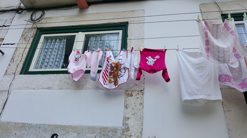Pink and white childrens shirts and a dishcloth hang from a washing line outside an old building