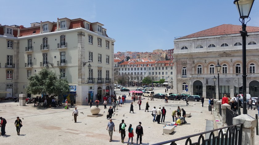 People mill about a city plaza ringed with historical buildings