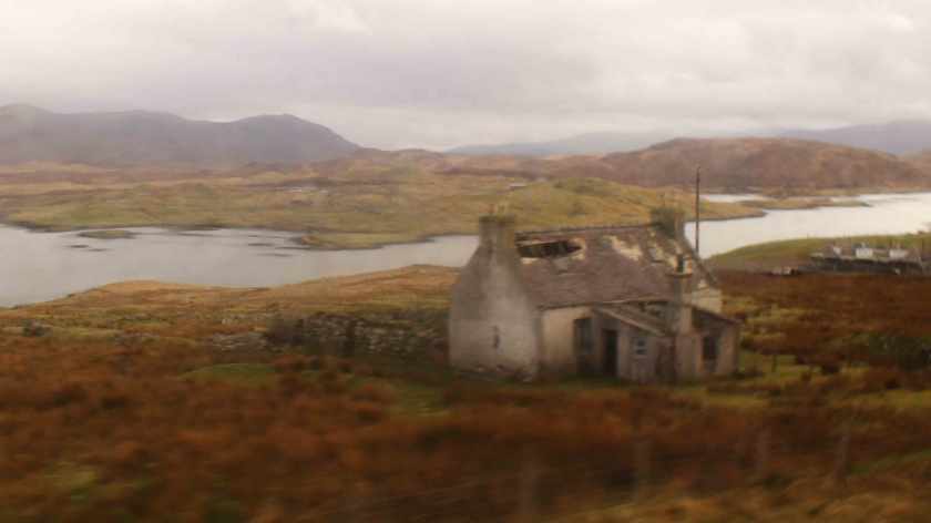 A broken down house at the edge of a river in a dry orange landscape.
