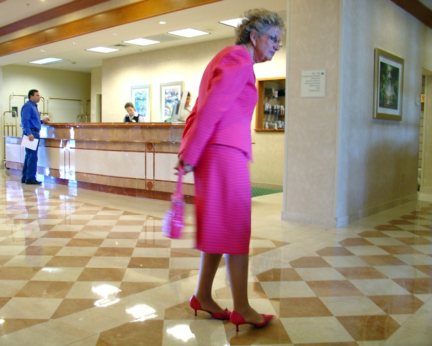 A woman in a bright pink suit in the marble lobby of a hotel