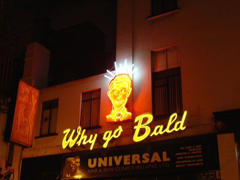 A neon sign with a full-haired man's head and the words Why go Bald?