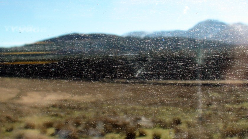 Through a smudged window a mountain landscape is visible.
