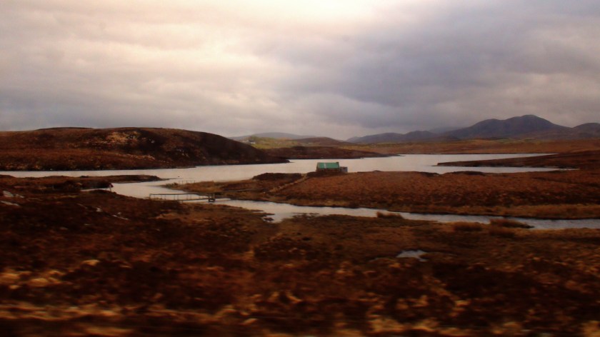 A copper coloured landscape with a winding stream and a tiny house in the background.