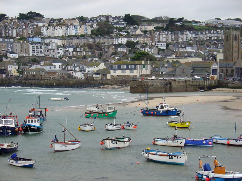 Colourful fishing boats sit on beach in front of a village on a hill