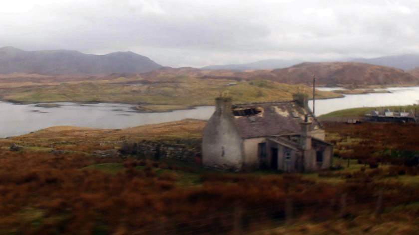 An abandoned house with broken roof in a foggy landscape at the edge of a creek.