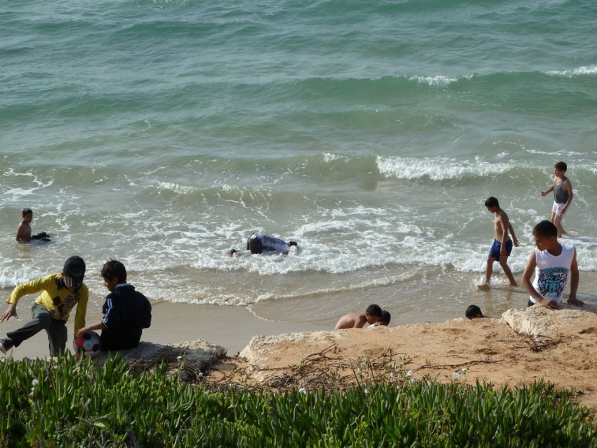 Boys play in the surf at the beach, one bending over with his head underwater