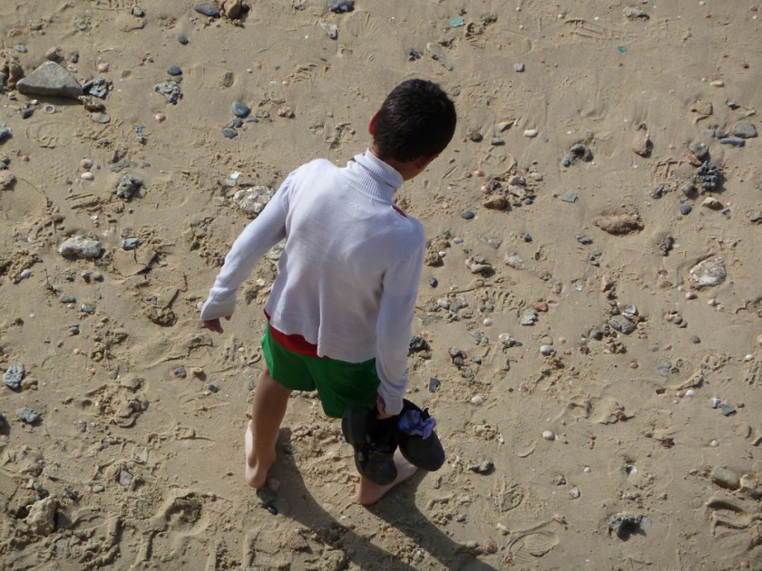 A boy seen from behind on a stoney beach