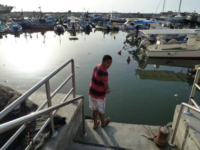 A young boy fishes in a port of small boats