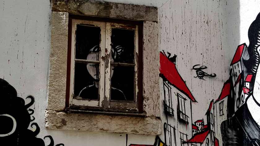 Red and black graffit against a peeling white building shows a face blocked by the windowsill