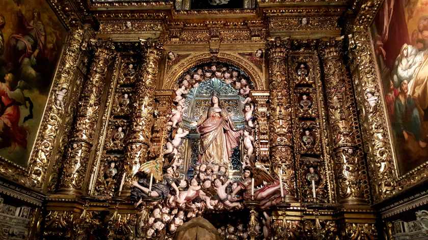 A plaster Virgin Mary surrounded by pink plaster cherubs in a gilted Church niche