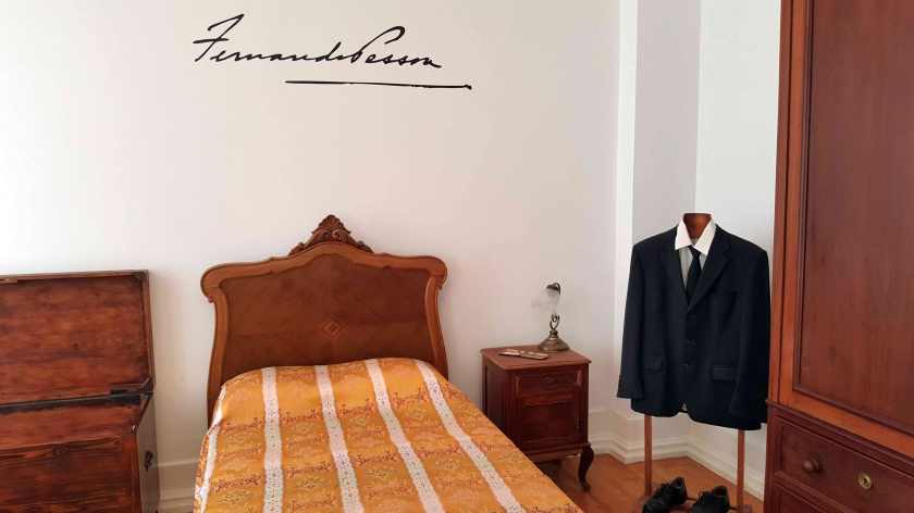The small bedroom of Fernando Pessoa with bed, chest, drawers and a black jacket and tie with white shirt on a mannequin