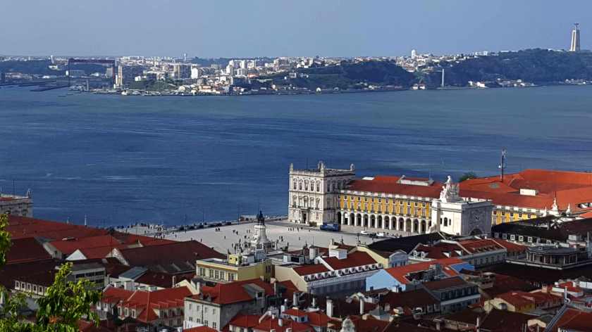 From high above, the edge of the city square, a river, and a far bank also with buildings