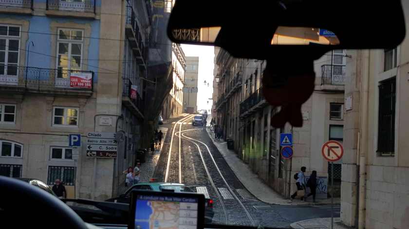 View from the windscreen of a car of a cobblestoned hill with tram tracks