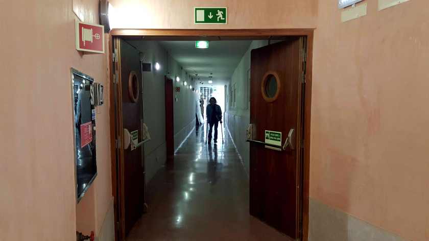 A man walking with crutches down an institutional hallway