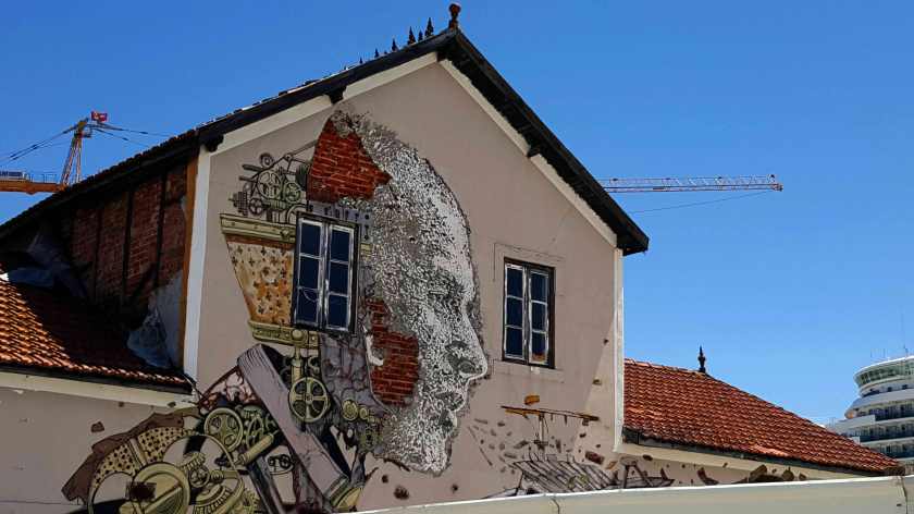 The side a building with a peeling mural showing a man's head composed of machine gears