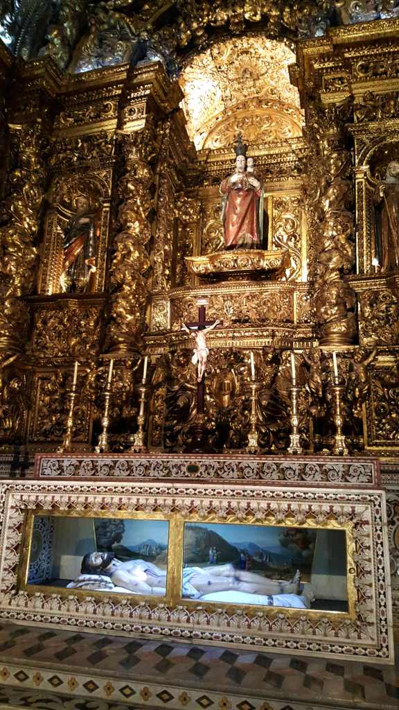 Plaster Jesus in a glass coffin lies below the Virgin Mary surrounded by gilt sculptures