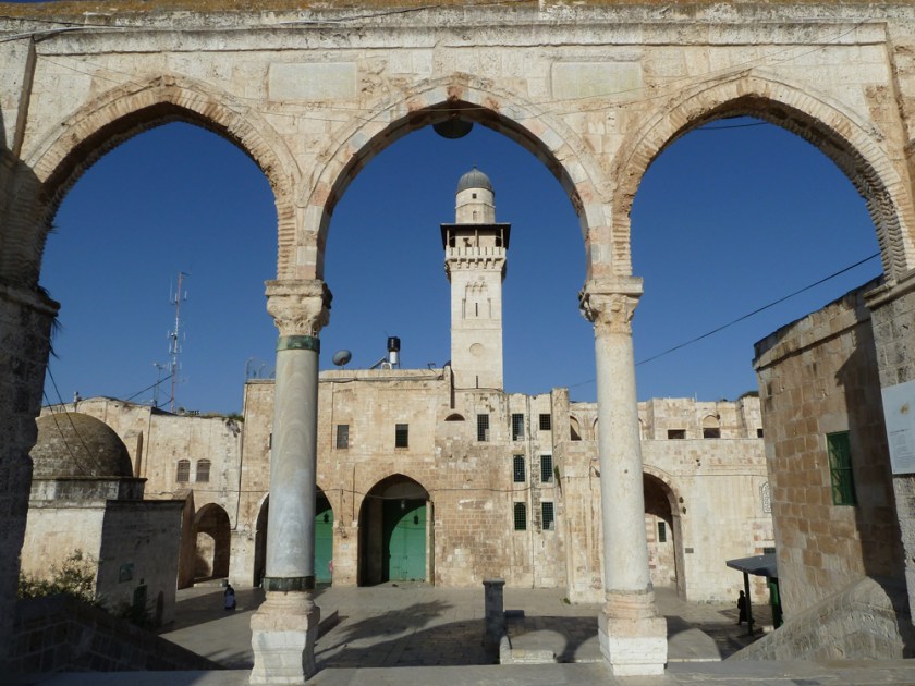 A mosque with minaret seen through ancient arches against a blue sky