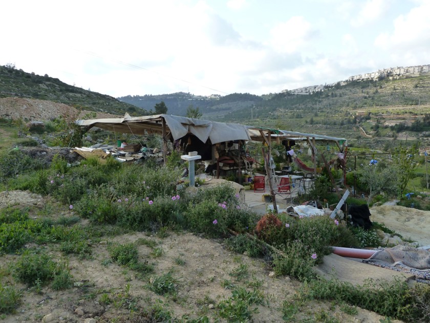 An open structure dwelling sits in the midst of a hilly landscape with settlements in the distance