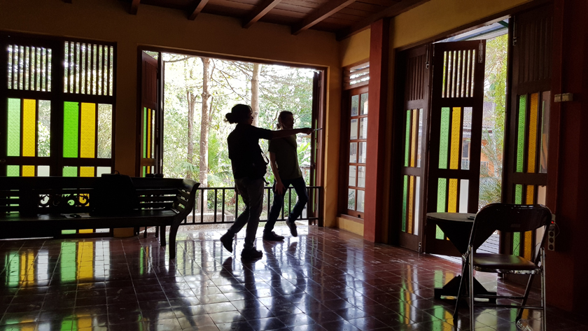 Silhoutted figures stand against the open doors of a square studio.