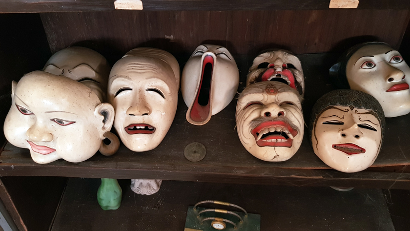 Seven Javanese theatrical masks, wooden painted white with red lips and black features, smile, frown, and grimace.