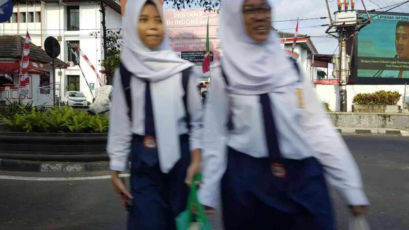 Two girls in school uniform, out of focus, cross the road.