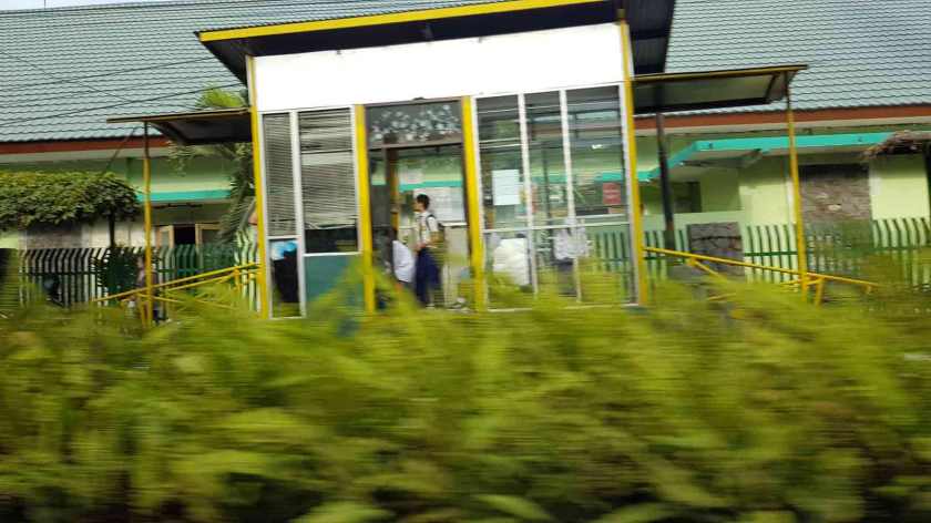 A young man in school uniform stands in a booth by the side of the road.