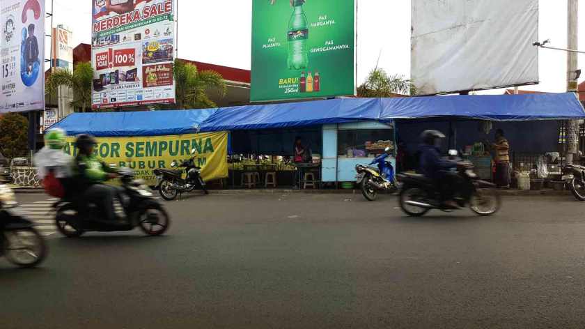 Motorbikes pass a restaurant stall beneath giant billboards