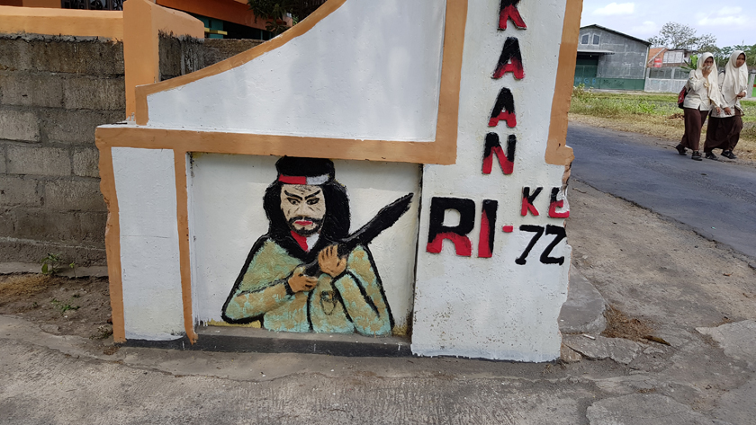 A mural of a warrior frescoed on a gate as two girls in Muslim dress pass