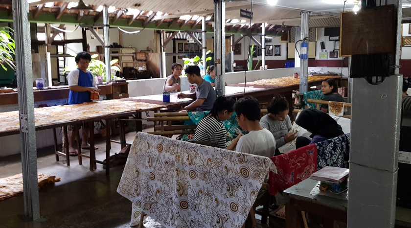 Male and female batik workers paint cloth in a shop