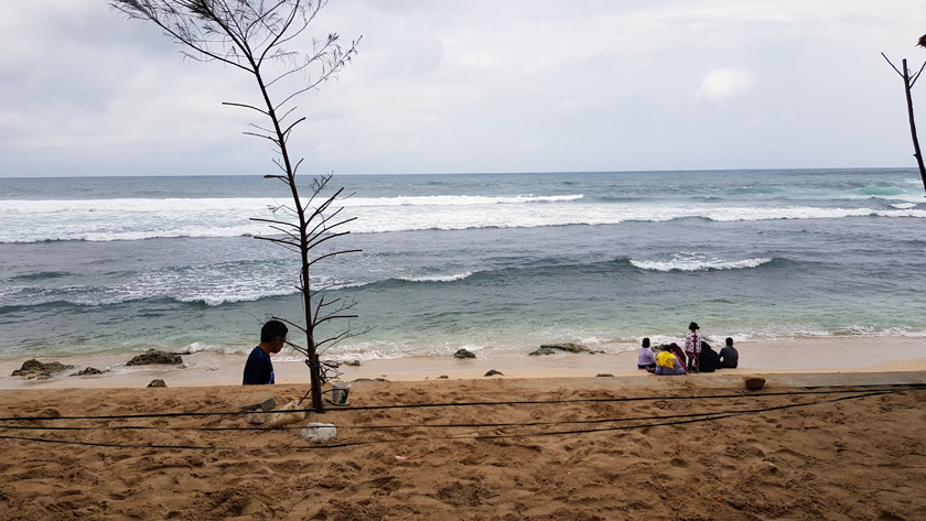 Seashore with figures huddled along the shore and a man walking past