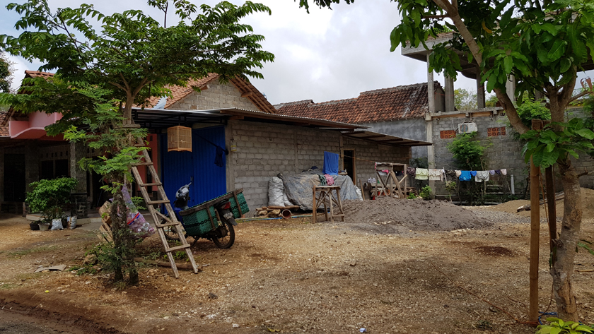Motorbike and ladder resting against a tree outside a concrete block rural house