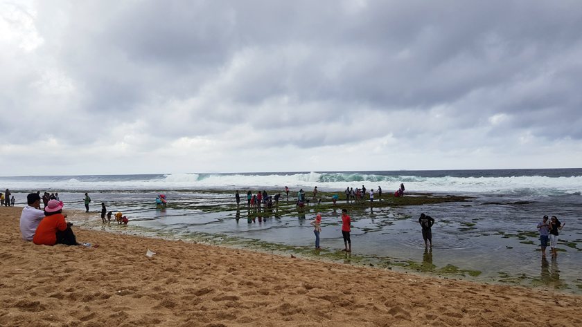 People wade along a seashore as the surf rolls in.
