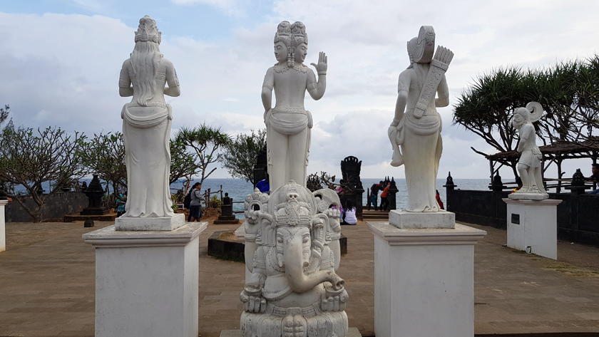 White stone sculptures of Buddhist deities and the Elephant God Ganesh stand on site at the edge of the sea.
