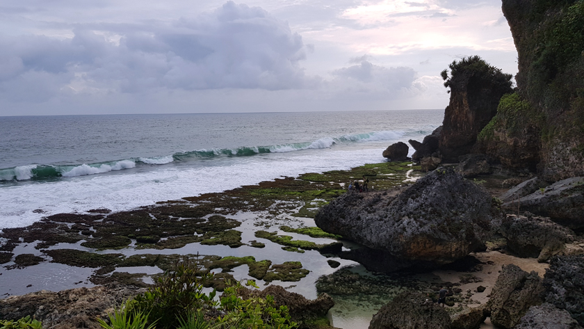 Sea rolls in along coastline with large rocks and jagged cliffs.