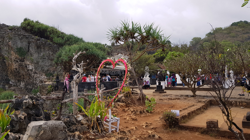 A heart shaped structure stands in front of Buddhist sculpture site perched int he mountain landscape