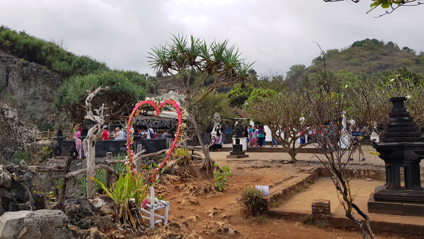 A heart shaped structure stands in front of Buddhist sculpture site perched int he mountain landscape
