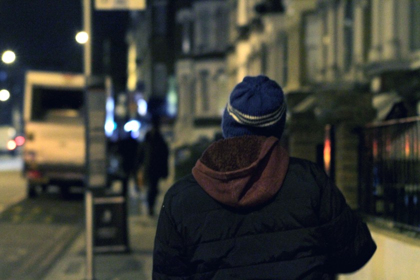 Seen from the back, a figure walks along an urban street at night.
