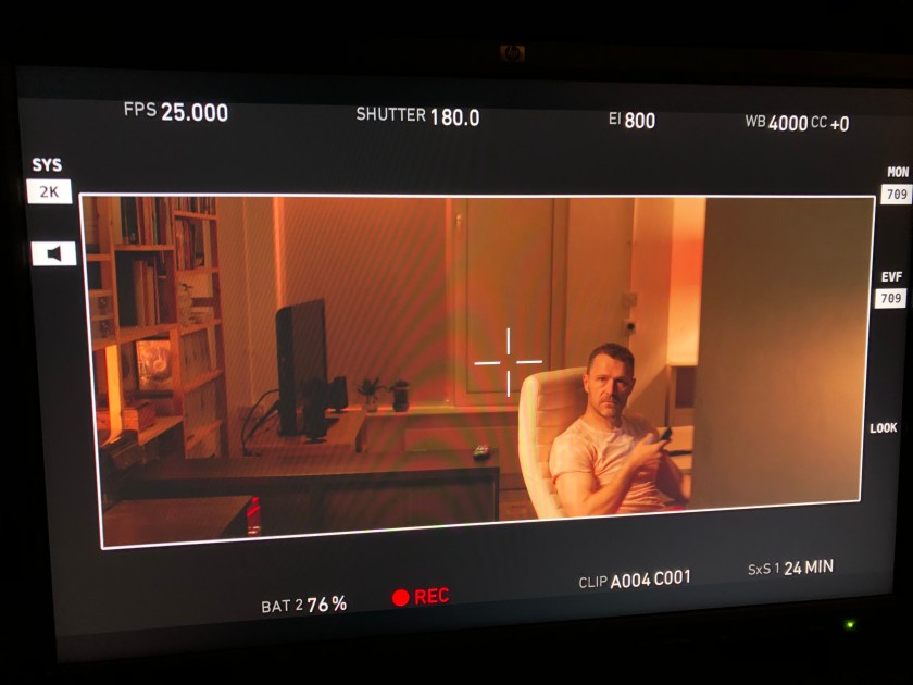 Anto turns around in his swivel chair, holding a remote.