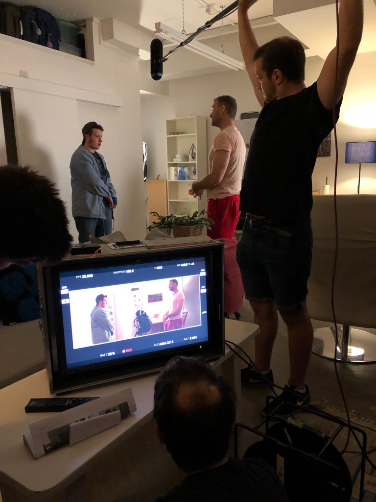 A boom operator holds the boom microphone above two actors.