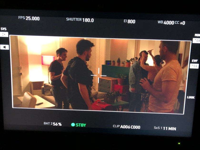 A makeup artist works on an actor while other people watch on set.