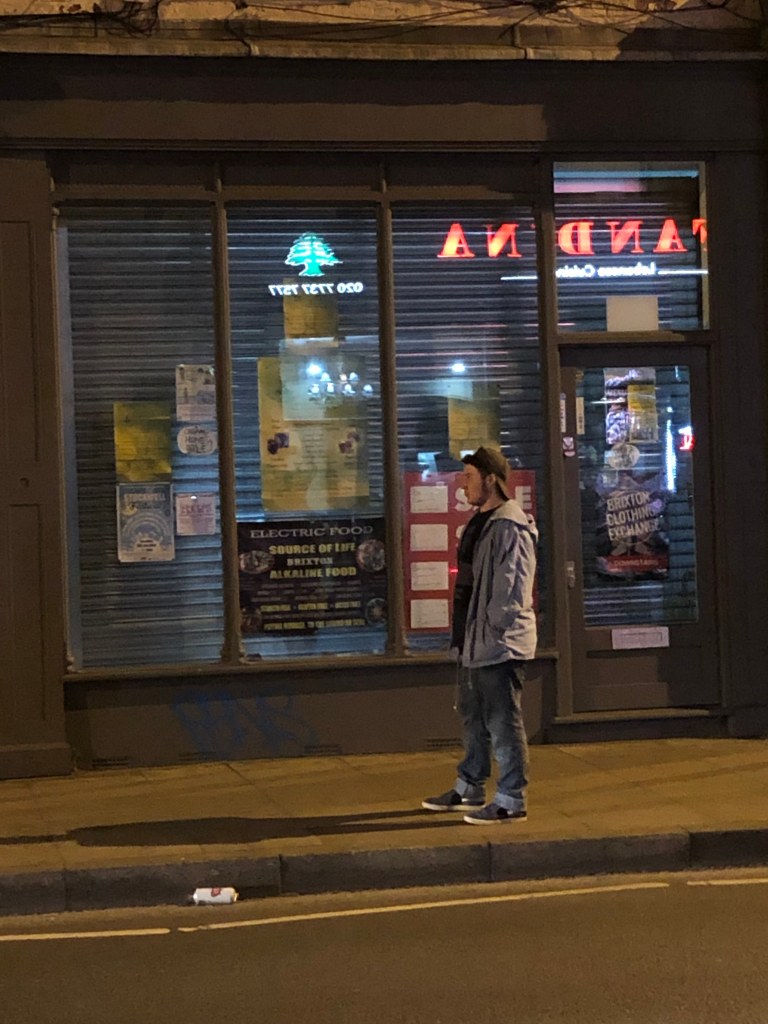 Orin walks along the street beside a storefront.