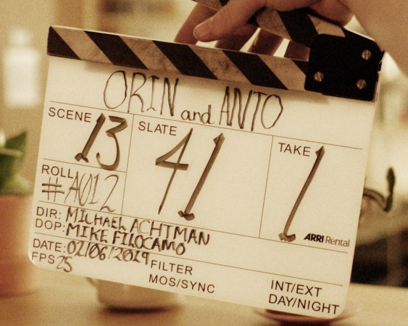 Hand holds a clapper board handwritten with Orin & Anto details