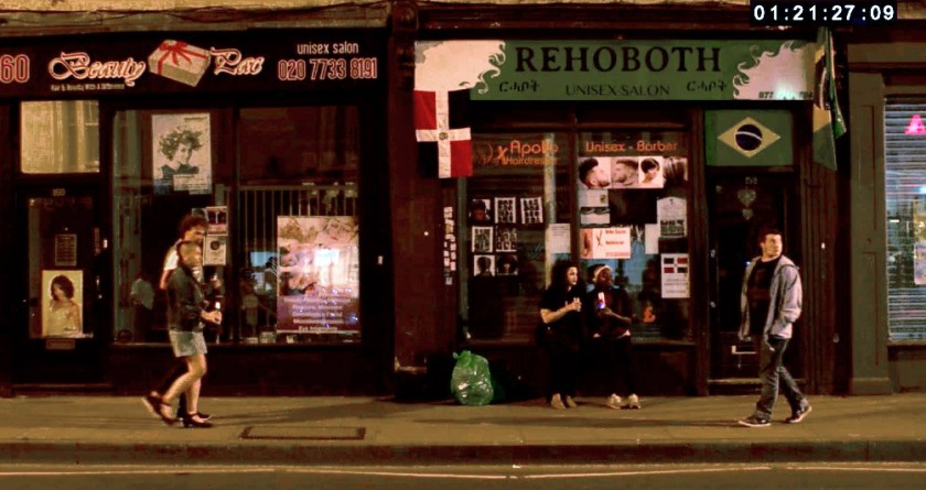 Urban street at night with Orin walking and passing other young people.