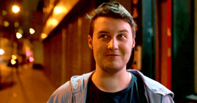 Smiling person wearing baseball cap on an urban street at night