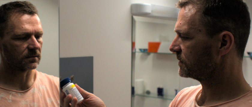 In the loo, Anto examines a container of tablets