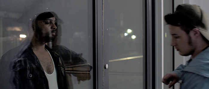 Orin and a man in studded leather on either side of a glass door